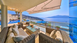 Un balcon agrémenté de meubles en osier, une piscine et une vue sur la mer et les collines.