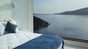 Une chambre avec une grande fenêtre donnant sur une mer calme et une côte rocheuse.