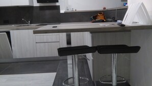 Una cocina moderna con televisor integrado, un lavamanos y dos taburetes de bar.