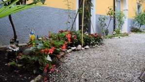 Un jardín con un sendero de grava, una estatua y un edificio de fachada amarilla y gris.