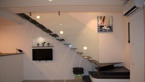 Una escalera moderna con barandillas de vidrio y diseño plano, que lleva a una plataforma con un televisor de pantalla plana y un pequeño estante con plantas.