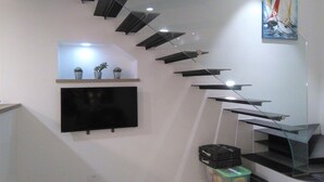 Una escalera moderna con barandilla de vidrio, un televisor de pantalla plana montado y un cuadro en la pared.