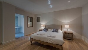 Un dormitorio con una cama de madera, dos mesitas de noche con lámparas, un espejo en la pared y una puerta que da al baño.