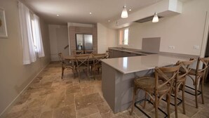 Una cocina moderna con una isla central, comedor con sillas e iluminación colgante.