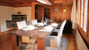 Una mesa de comedor de madera dispuesta con platos, vasos y cubiertos, con sillas acolchadas a cada lado, en una habitación con paredes de madera y chimenea.