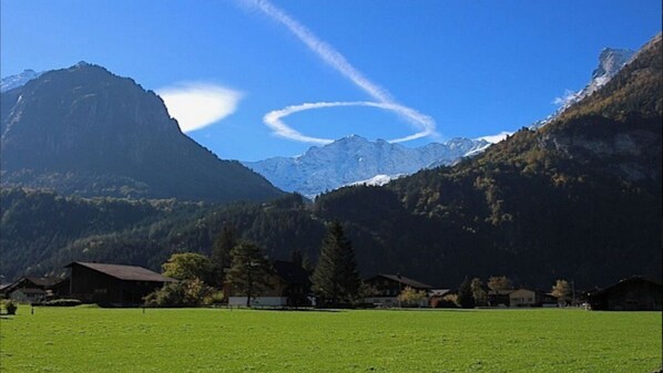 Eine Berglandschaft mit blauem Himmel, einer ringförmigen Wolkenformation und Häusern im Vordergrund.