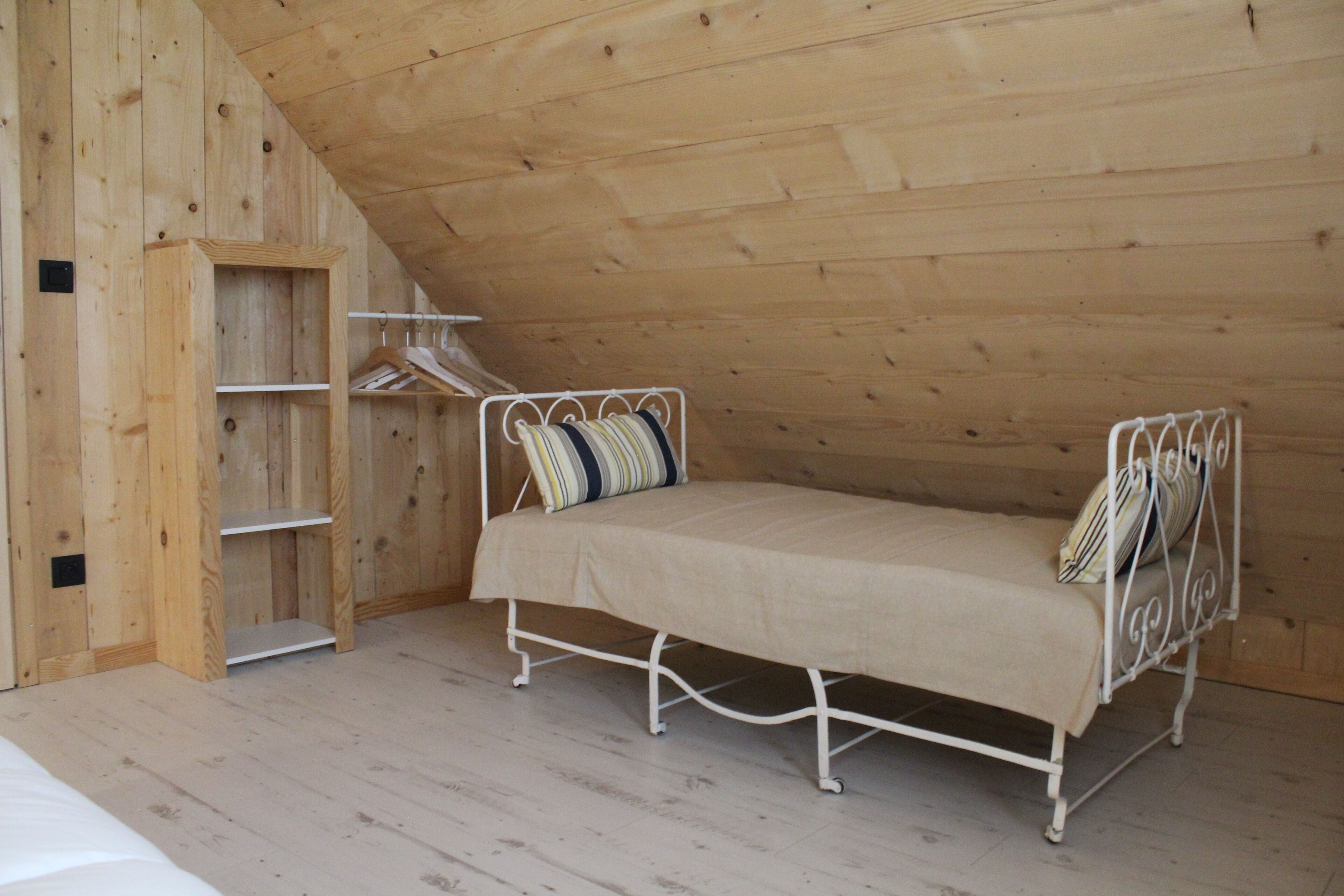 Una habitación pequeña con cama individual, techo inclinado y paredes de madera.