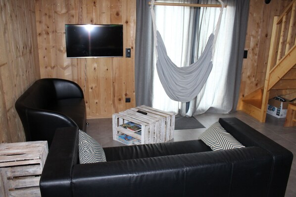 A cozy living room with a black leather sofa, a wooden coffee table, and a television mounted on the wall.