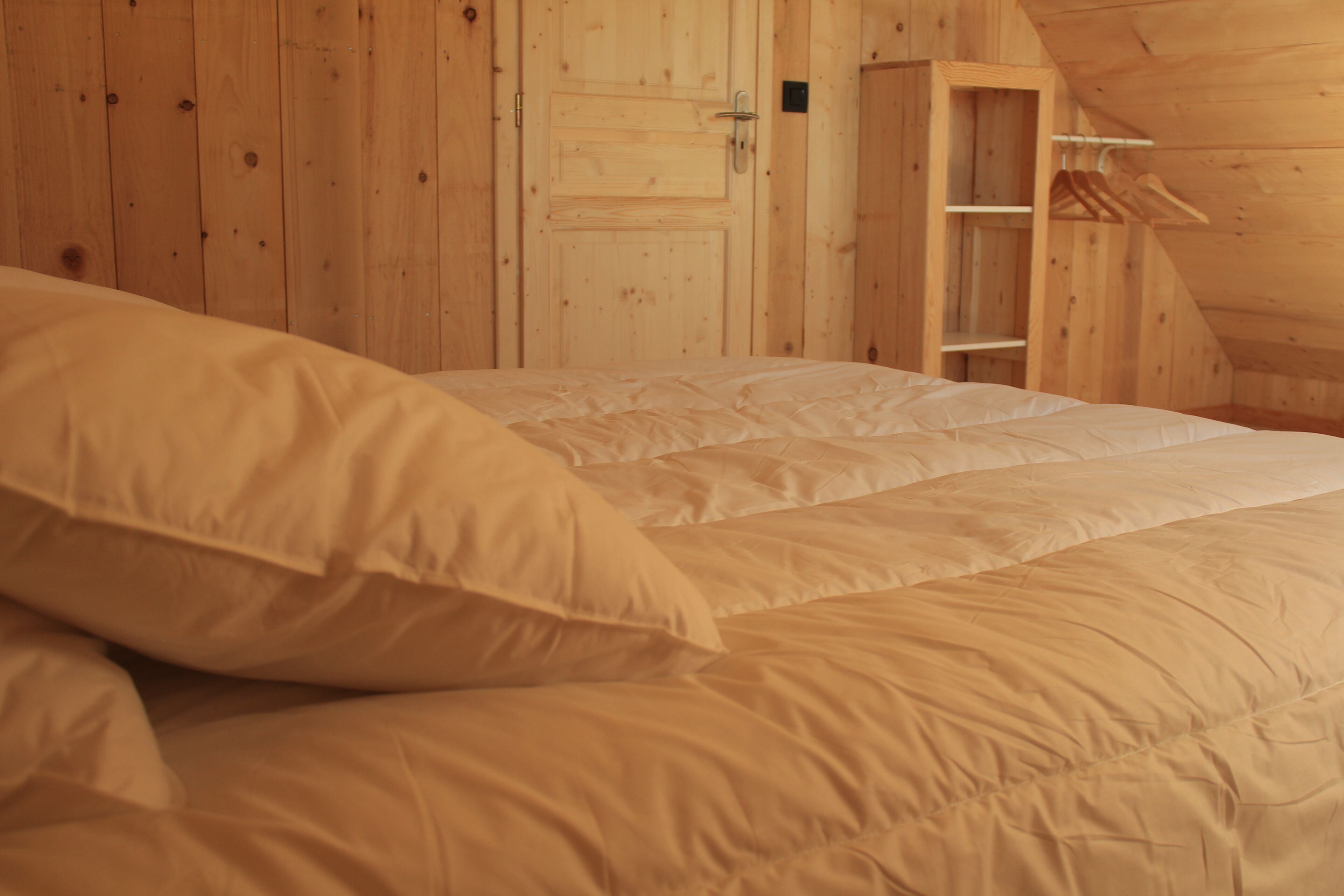 A bedroom with a wooden ceiling and walls, a bed with white bedding, and a wooden wardrobe with a hanging rack.