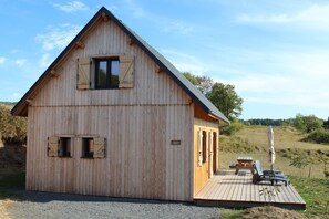 A wooden cabin with a sloped roof, a wooden deck, a picnic table, and an umbrella.