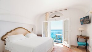 A bedroom with a bed, a nightstand, a small table with a lamp, a chair, and a balcony with a view of the sea. - M'Illumino d'Immenso Studio with sea view (Praiano)