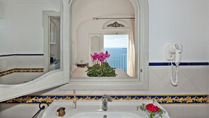 A bathroom with a large mirror, a sink, a hairdryer, and a view of the sea through an open door. - M'Illumino d'Immenso Studio with sea view (Praiano)