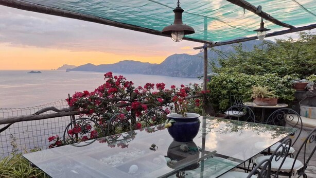 A glass table with chairs under a pergola, overlooking a body of water and mountains. - M'Illumino d'Immenso Studio with sea view (Praiano)