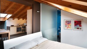 A bedroom with a wooden ceiling, a bed, a bedside table, and a view of a kitchen and bathroom through an open door. - Sant Agostino Loft in historical city center (Catania)