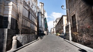 A narrow street with stone pavement, ornate metal gates, and historic buildings. - Sant Agostino Loft in historical city center (Catania)