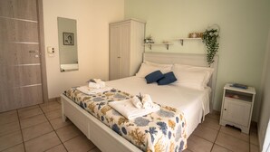 A bedroom with a bed, a wardrobe, a bedside table, and a hanging plant. - Apartment Salgari Ponente (Marina di Ragusa)