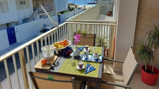 A balcony with a table set for breakfast, overlooking a residential area and the sea. - Apartment Salgari Ponente (Marina di Ragusa)