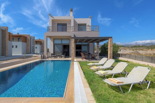 A modern pool area with lounge chairs, a covered seating area, and a two-story building with stone accents.