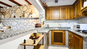 A kitchen with granite countertops, wooden cabinets, a stone backsplash, and a small wooden table with fruit.