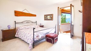 A bedroom with a bed, nightstands, a hanging artwork, a framed picture, and a balcony with a view.