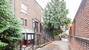 Une ruelle étroite bordée d’immeubles en briques, avec un escalier et un grand arbre.