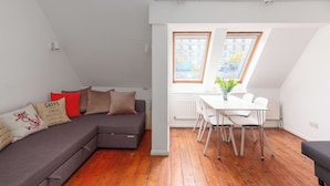 Un appartement moderne avec un canapé gris, une table à manger avec des chaises et une grande fenêtre laissant entrer la lumière naturelle.
