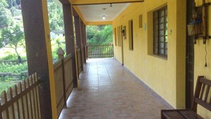 A covered corridor with tiled flooring, wooden benches, and a view of greenery outside. - Recanto José Augusto (Mairiporã)