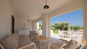 A spacious living area with a sofa, chairs, and a table, featuring large windows with a view of greenery and a clear sky. - Terra Mater - exclusive cottage (Ostuni)