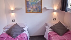 Deux lits simples avec des oreillers, un tableau au mur et des lampes fixées au mur.
