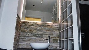 Une salle de bain avec un mur en pierre, un lavabo blanc et un miroir.