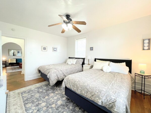 A bedroom with two beds, a ceiling fan, and a small table with a lamp.