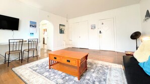 A spacious living room with a wooden coffee table, a TV mounted on the wall, and a sofa. - 6649 2W | Central St. Louis Beauty (St. Louis)