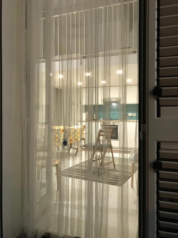A room with a large window covered by sheer curtains, a wooden chair, and a table.