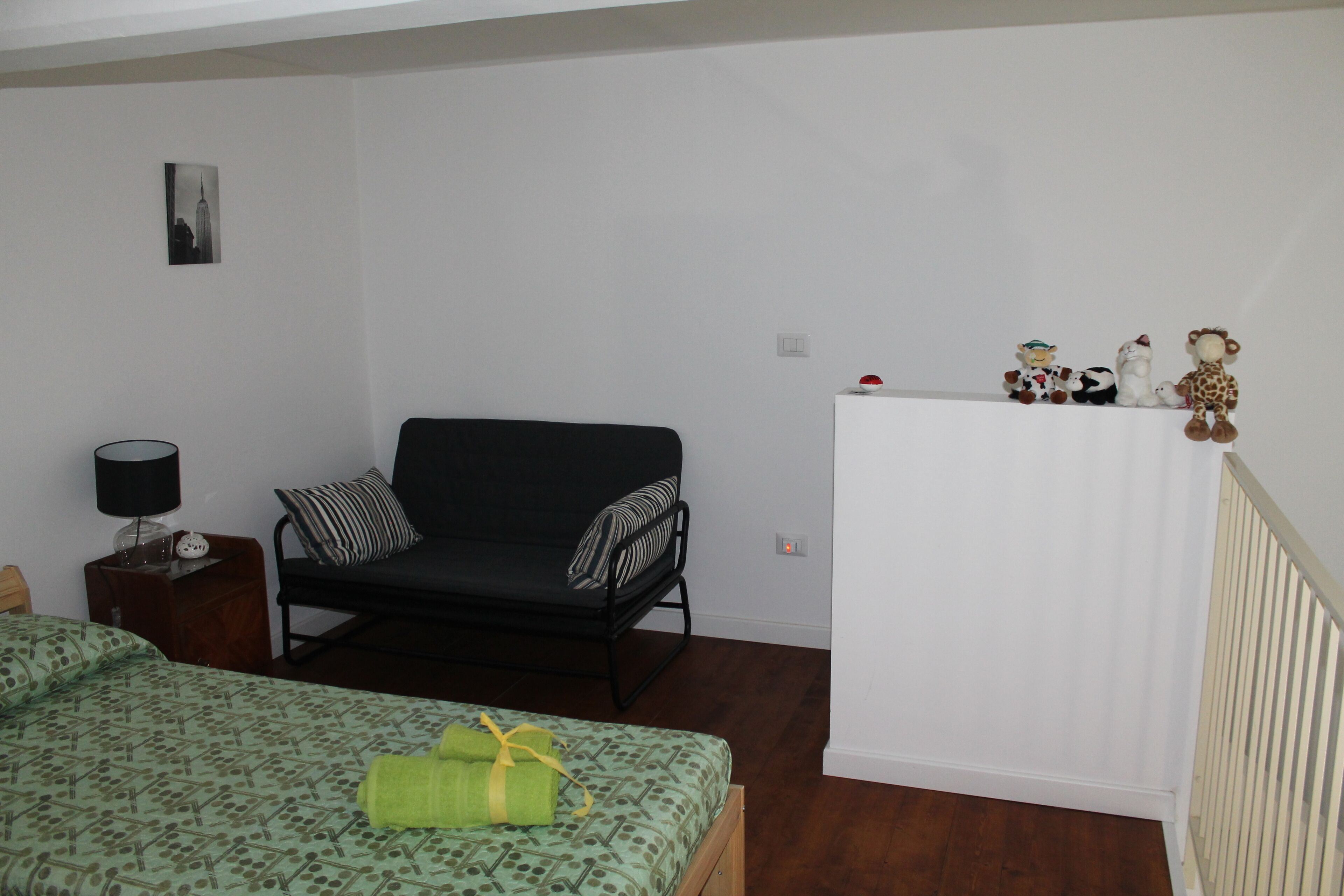 Ein Schlafzimmer mit einem Bett, einem Sofa, einem Nachttisch, einer Lampe und einem an der Wand befestigten Regal mit Figuren.