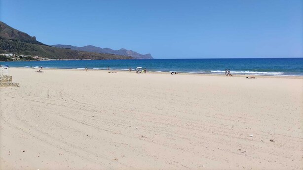 Une vaste plage de sable fin, sous un ciel bleu dégagé et une mer calme.