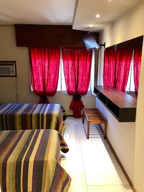 A hotel room with two beds, a TV mounted on the wall, and a small wooden table. - Hotel Riviera (Villa Carlos Paz)