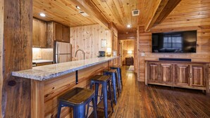 Un interior de madera con una zona de cocina, taburetes de bar y un televisor.