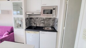Una kitchenette compacta con microondas, lavamanos y refrigerador. Hay un sofá rosa y un gabinete de vidrio con vista.