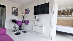 Una sala de estar moderna con un sofá púrpura, una zona de comedor con sillas moradas, un televisor de pantalla plana y un elemento decorativo en la pared.
