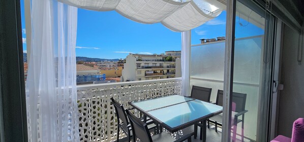A balcony with a glass table and chairs, white lattice partition, and a view of buildings and hills. - Nice center: two-room apartment with bedroom, terrace, wifi, internet, air cond. (Nice)