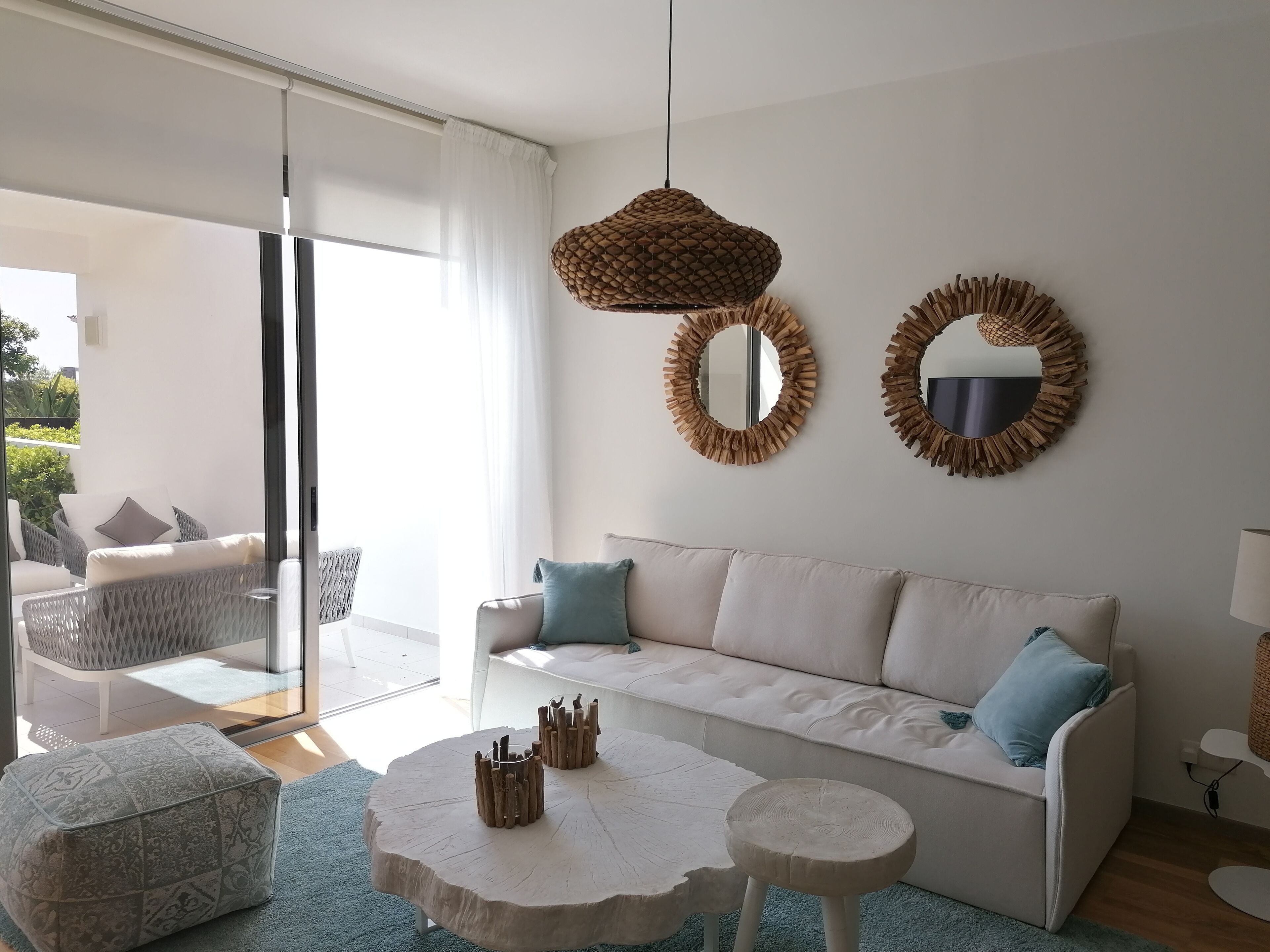 A modern living room with a white sofa, two round mirrors, a round wooden coffee table, and a wicker hanging light fixture.