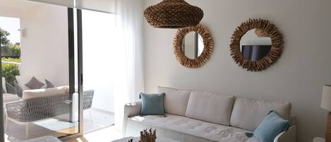A modern living room with a white sofa, two round mirrors, a round wooden coffee table, and a wicker hanging light fixture.