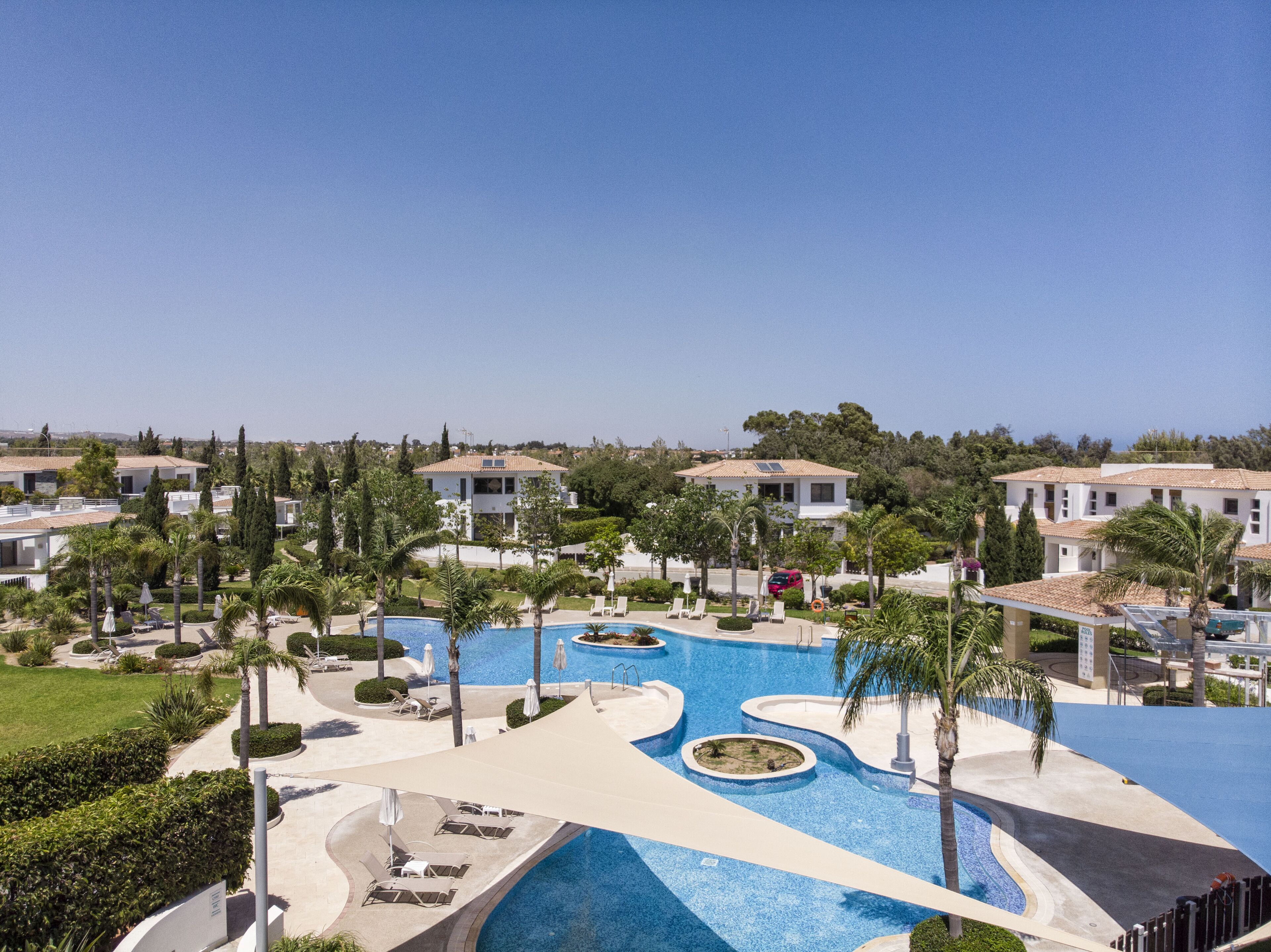 A resort with a large swimming pool, palm trees, and villas.