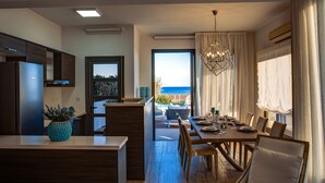 A modern kitchen with a view of the sea, a dining area with a table set for four, and a balcony with outdoor furniture. - Atlantis Gardens (Mazotos)