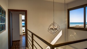 A staircase with a view of the beach, a hanging light fixture, and a door leading to another room. - Atlantis Gardens (Mazotos)