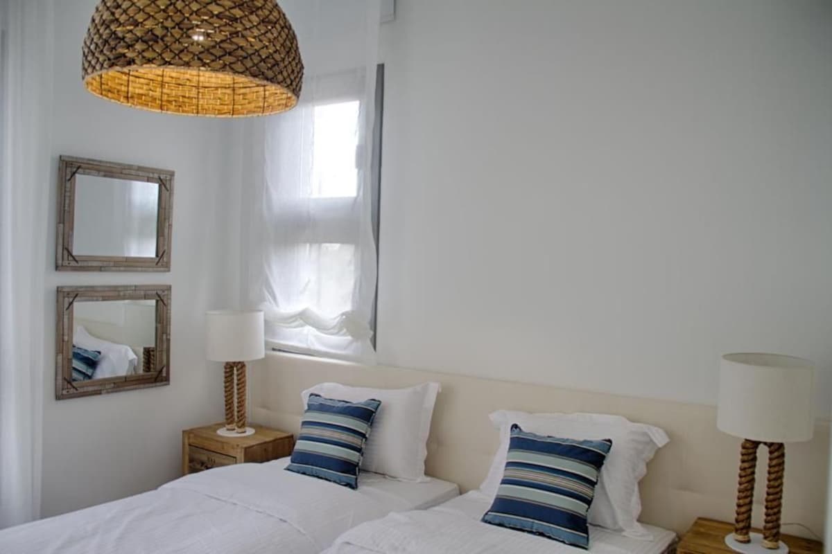 Ein Schlafzimmer mit zwei Betten, einem großen Fenster und einer Pendelleuchte.