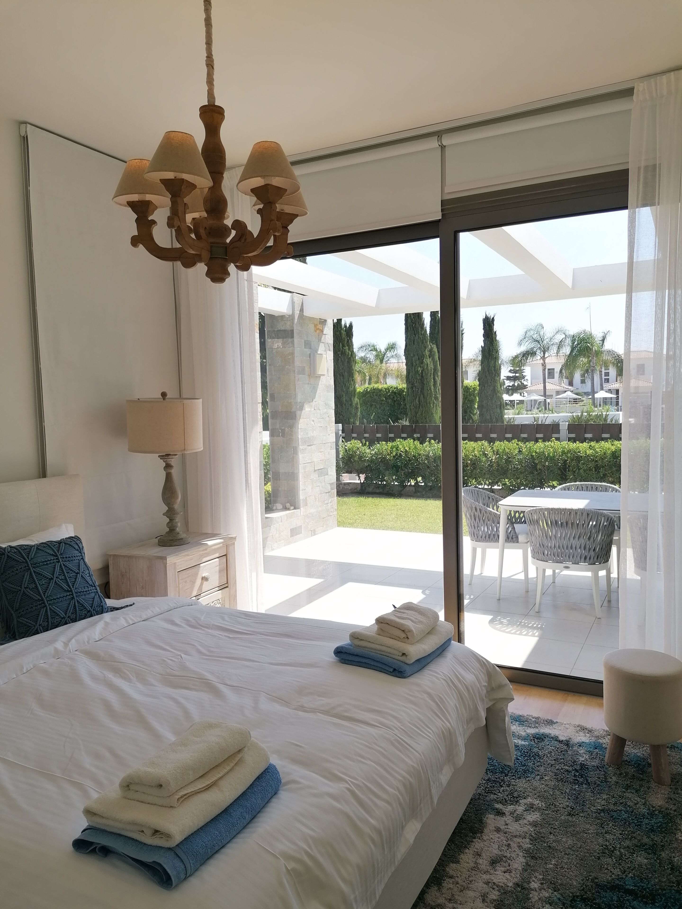 Ein Schlafzimmer mit einem großen Bett, einer Chandelüster, einem Nachttisch und Blick auf eine Außenpatio mit Tisch und Stühlen.