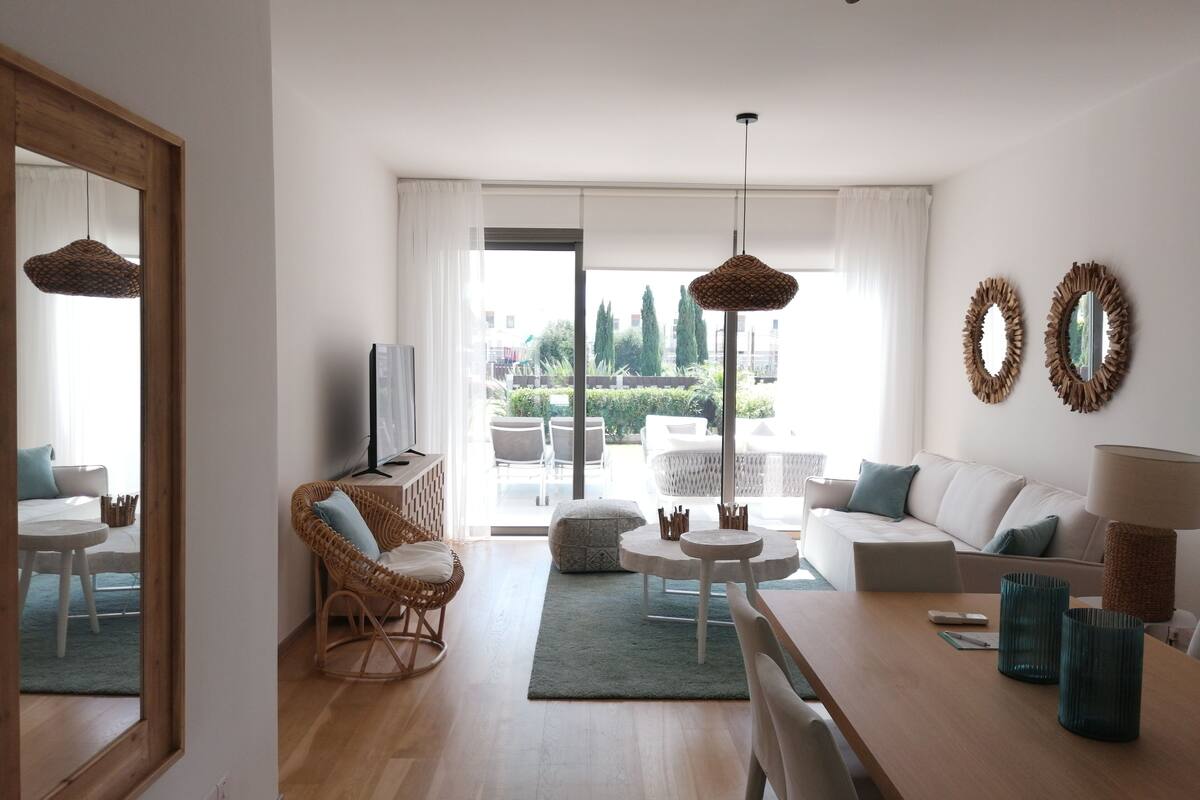 Ein modernes Wohnzimmer mit einer Couch, einem Esstisch, Korbstühlen und einem Fernseher.