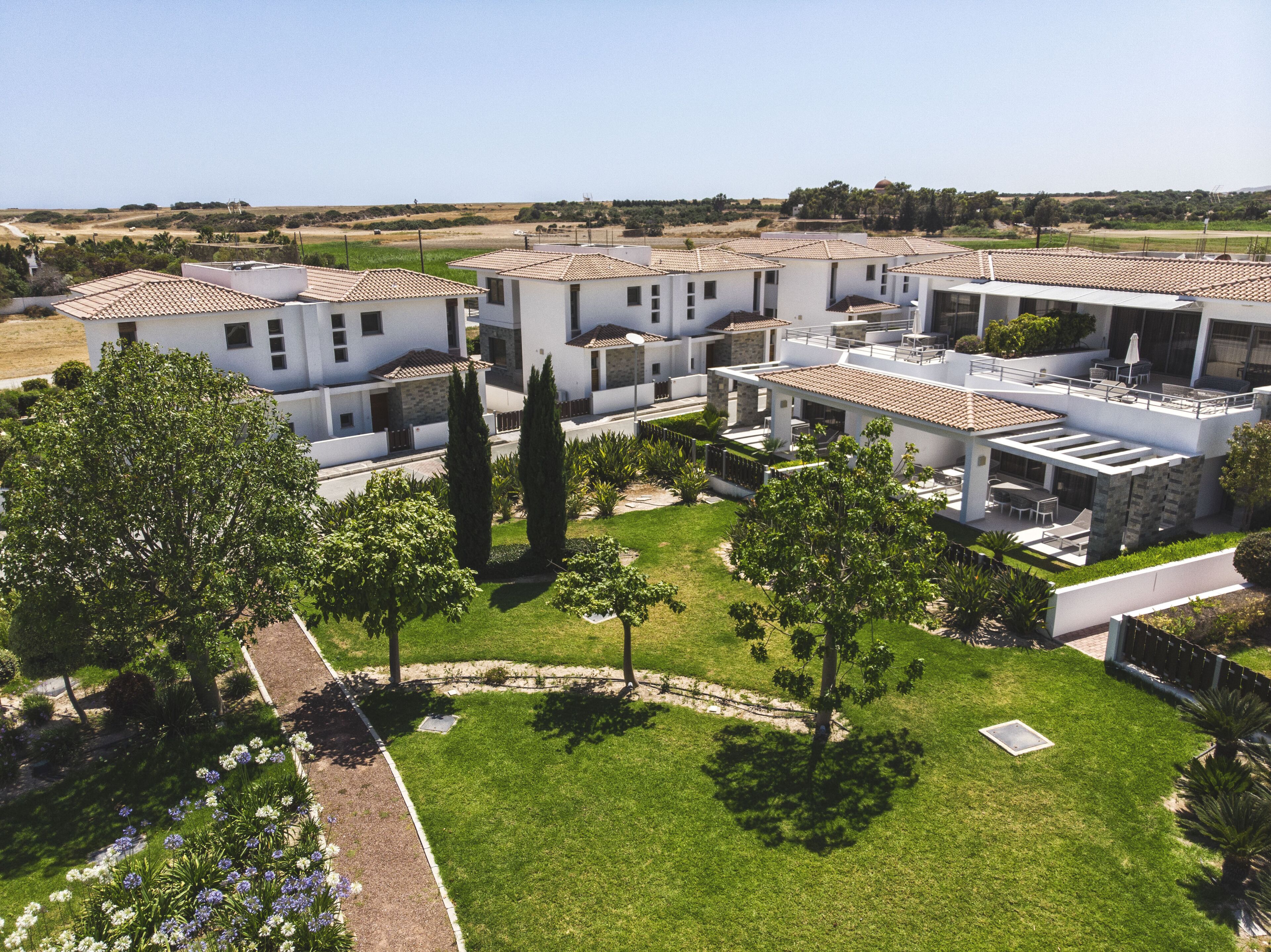 A residential complex with multiple two-story houses, each featuring a tiled roof, a balcony, and a small garden area.