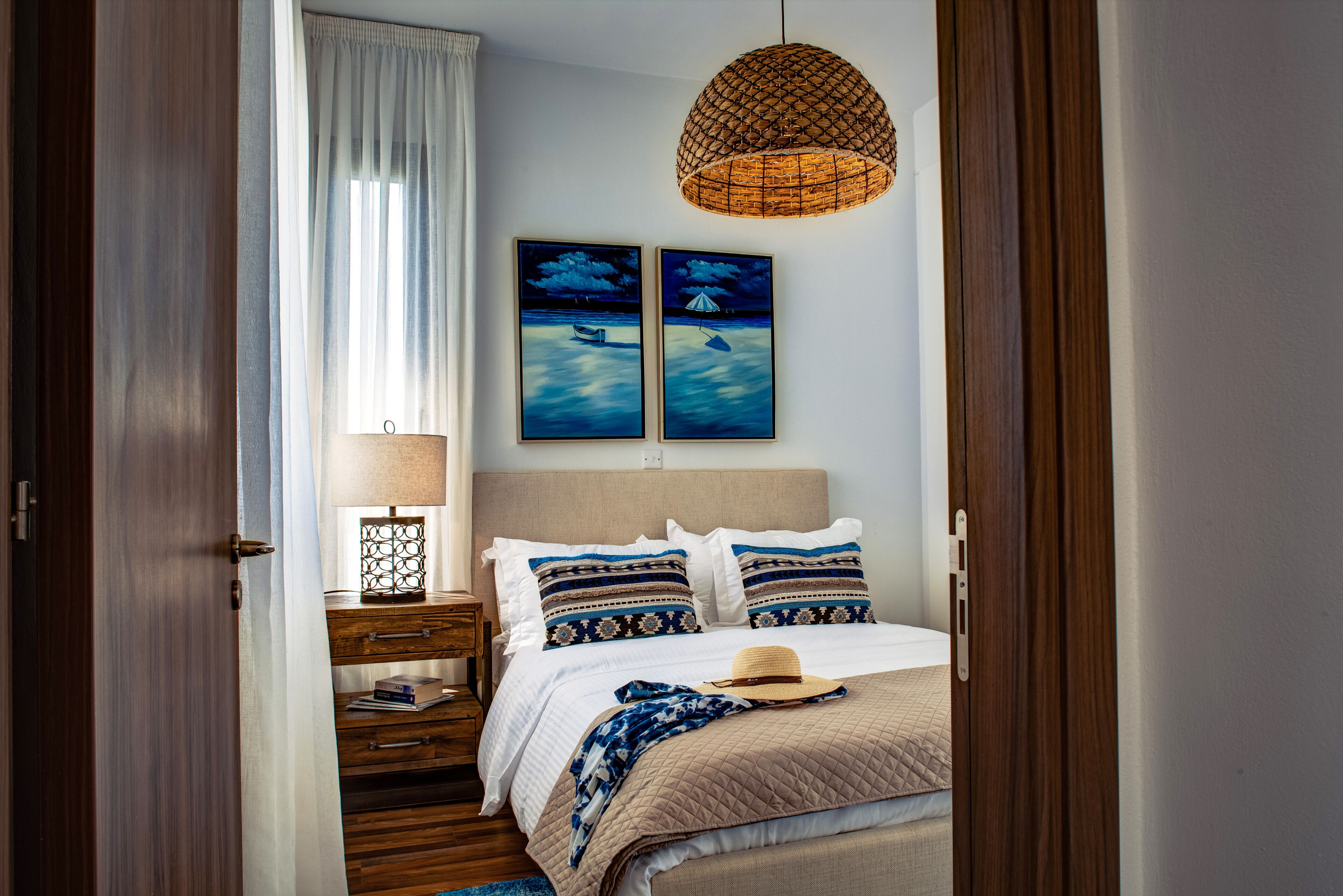 Un dormitorio con cama, mesita de noche, lámpara y dos cuadros en la pared.